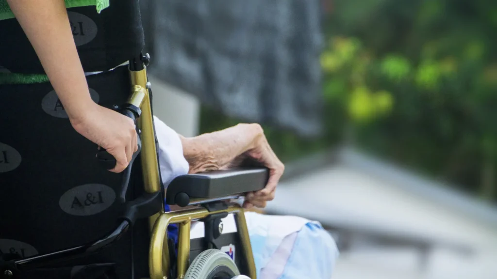 Elderly person’s hand resting on the armrest of a wheelchair.